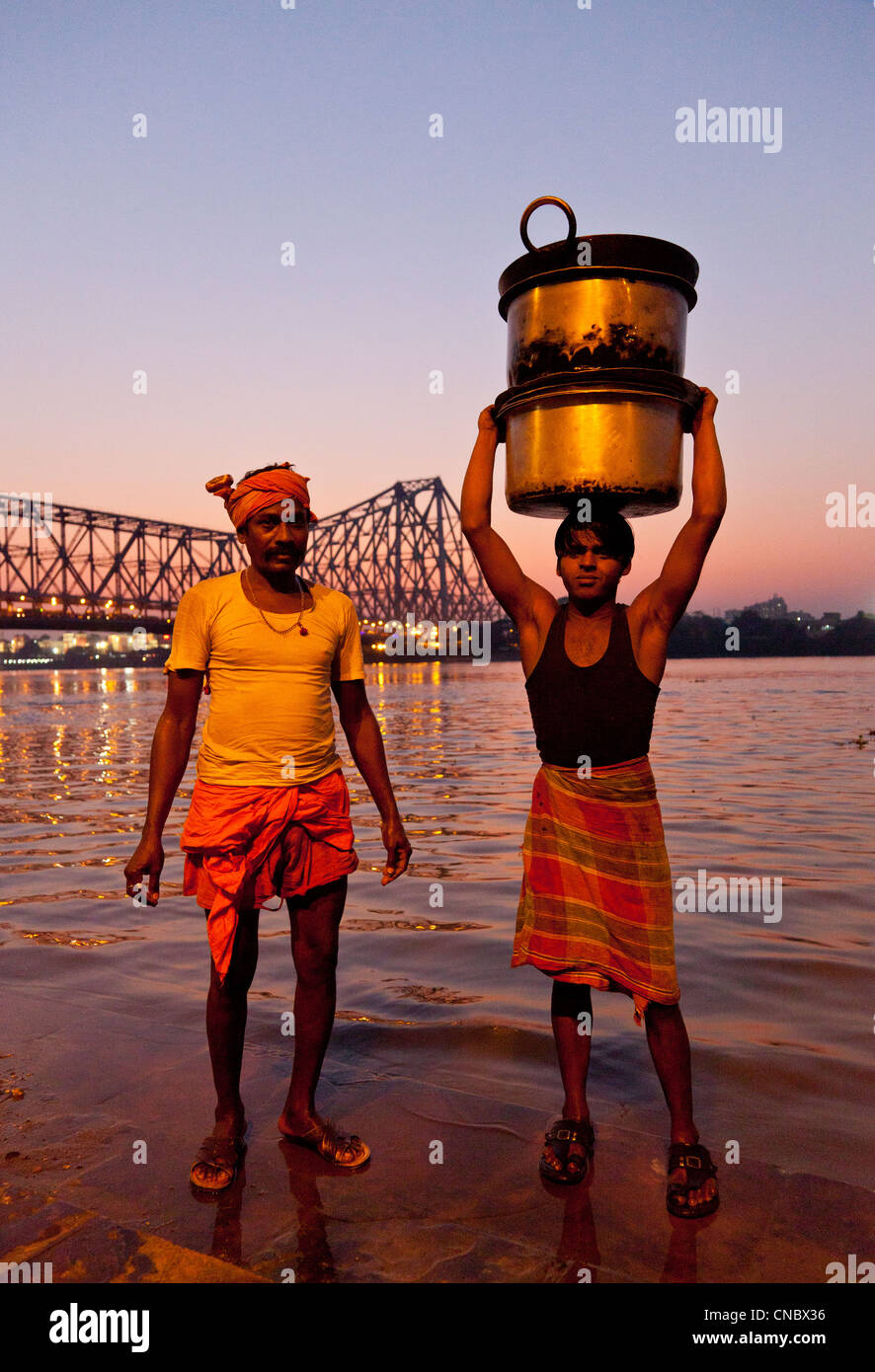 L'Inde, le Bengale occidental, Kolkata (Calcutta), deux hommes avec des ustensiles à Hooghly River avec Howrah Bridge au-delà Banque D'Images