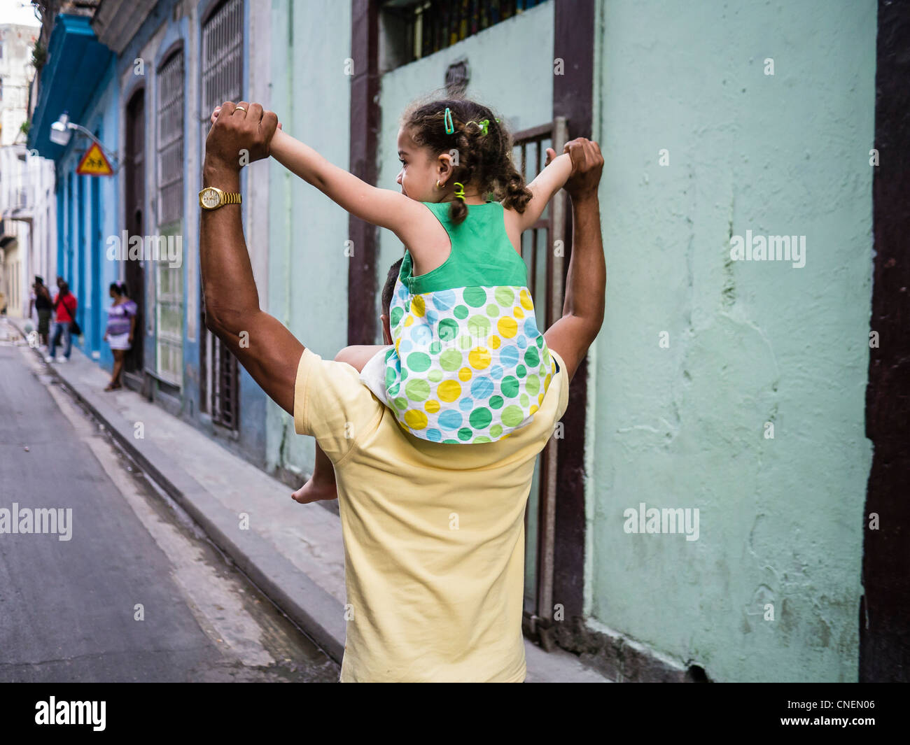 Un père cubain à La Havane porte sa petite fille sur ses épaules avec ses deux mains et tenus ensemble au-dessus de sa tête. Banque D'Images