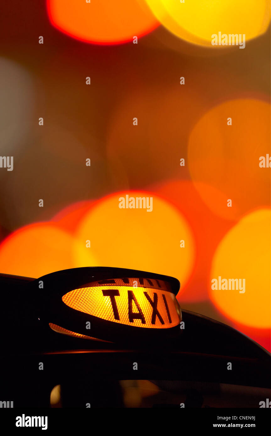 Un taxi londonien allumé dans la nuit avec un signe de-l'accent lumières dans l'arrière-plan Banque D'Images