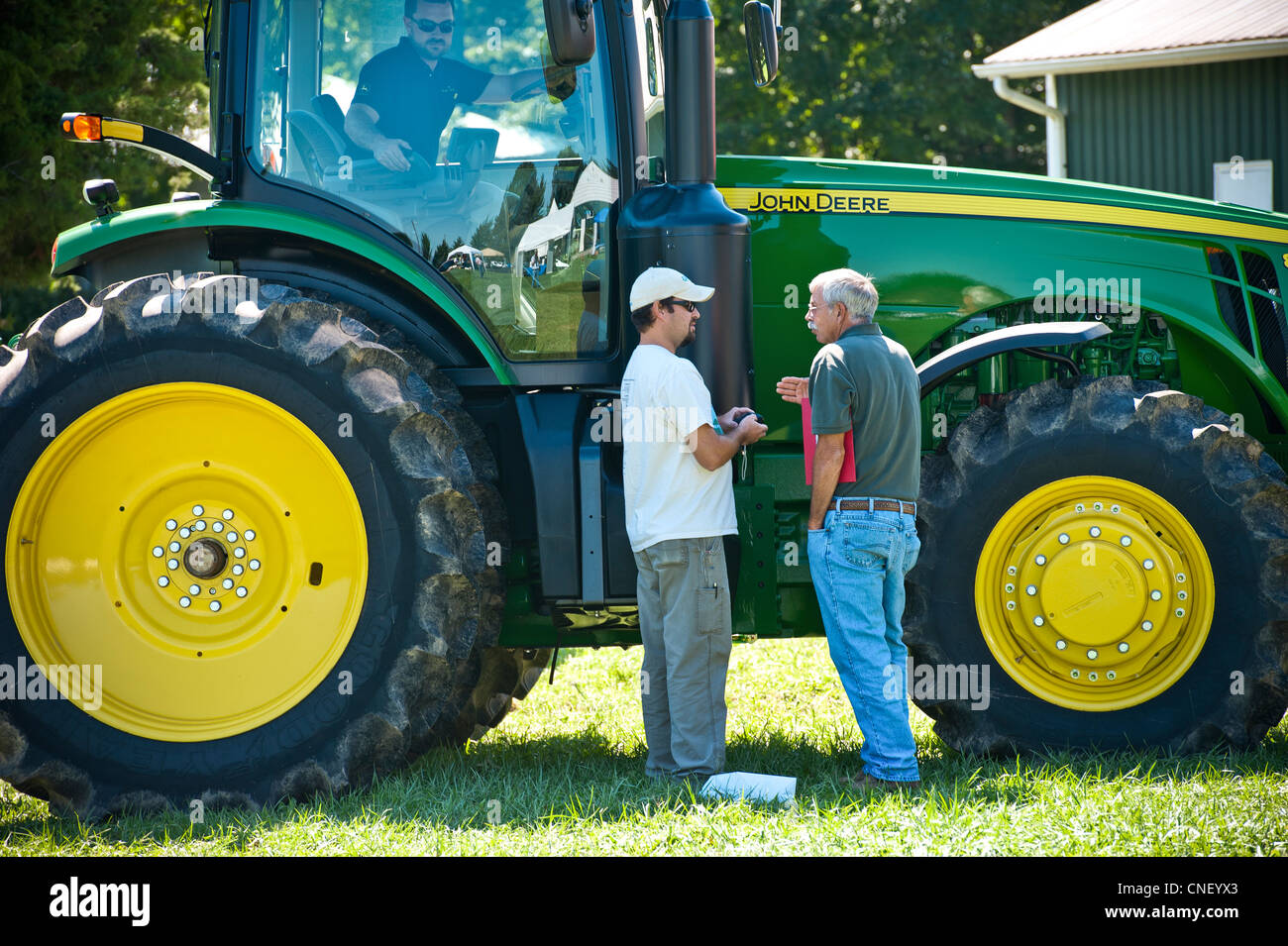 Deux hommes debout à côté d'un grand tracteur et un homme monté à l'intérieur du tracteur Banque D'Images