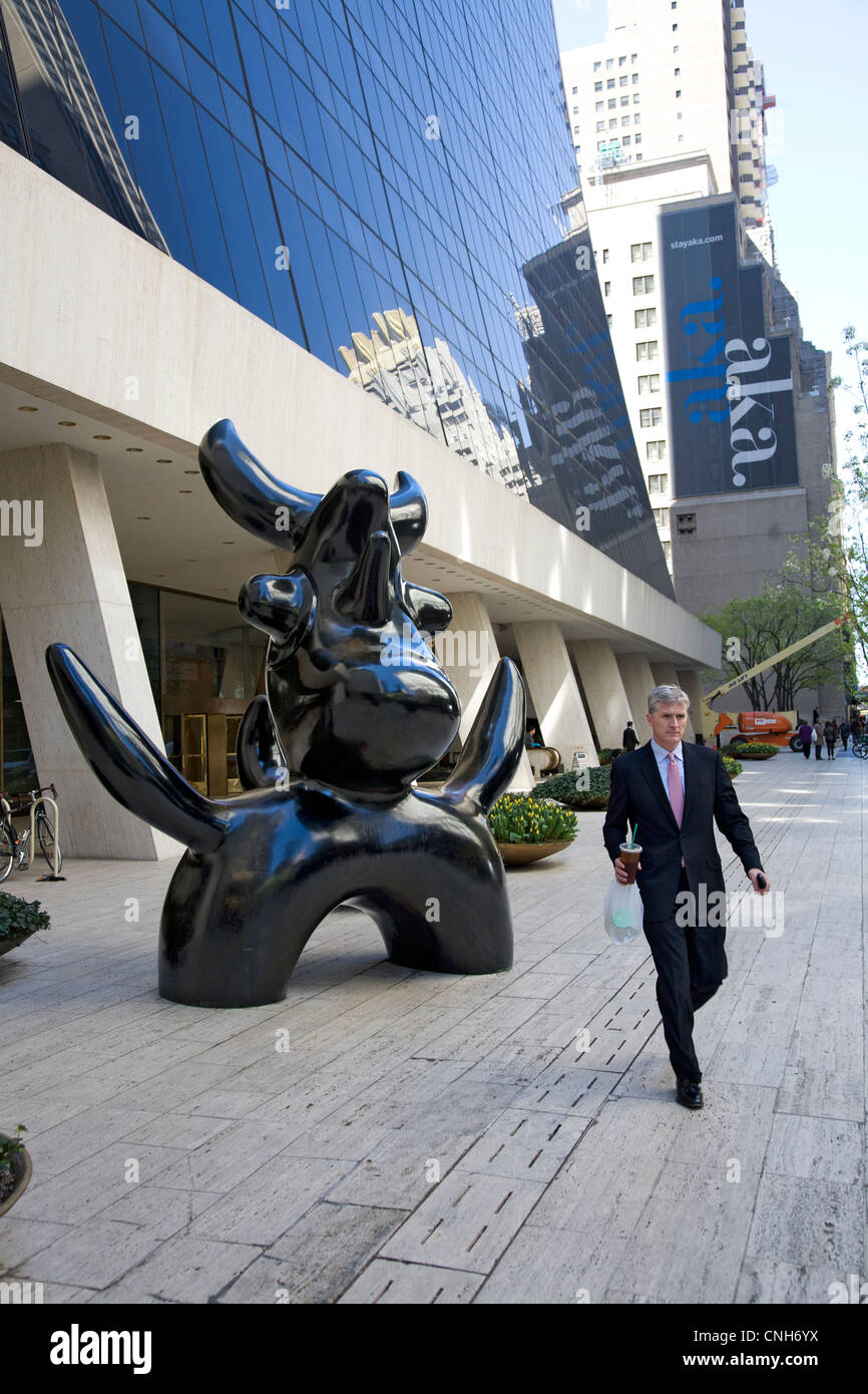 Homme marche par Joan Miro's 'oonbird' sculpture (1966), situé sur la place de l'immeuble sur Solow 58th Street à New York Banque D'Images