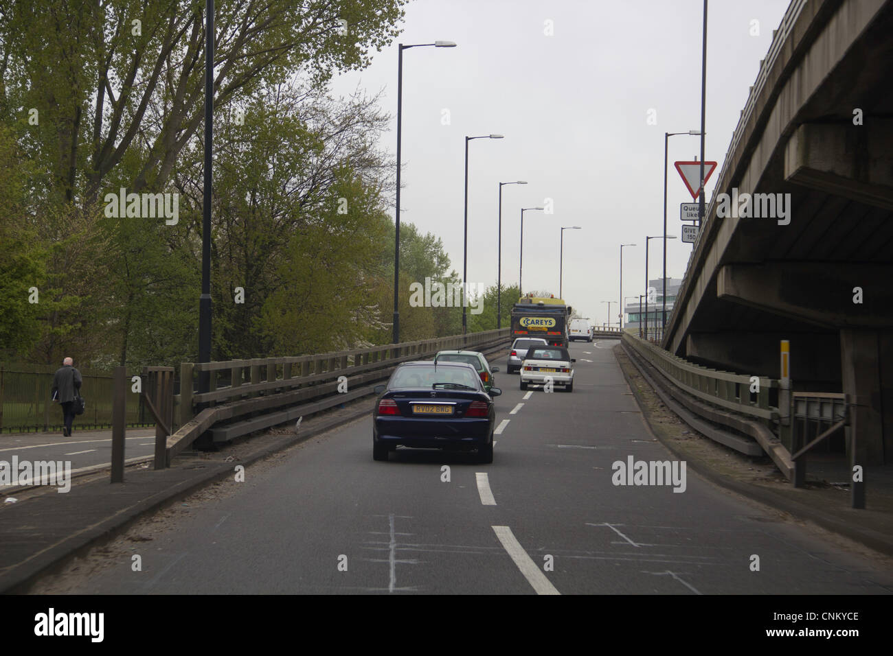 Voitures sur une rampe jusqu'à Londres pour rejoindre la route principale, entouré par des arbres sur le côté et une voie de service. Piliers de soutien visible. Banque D'Images