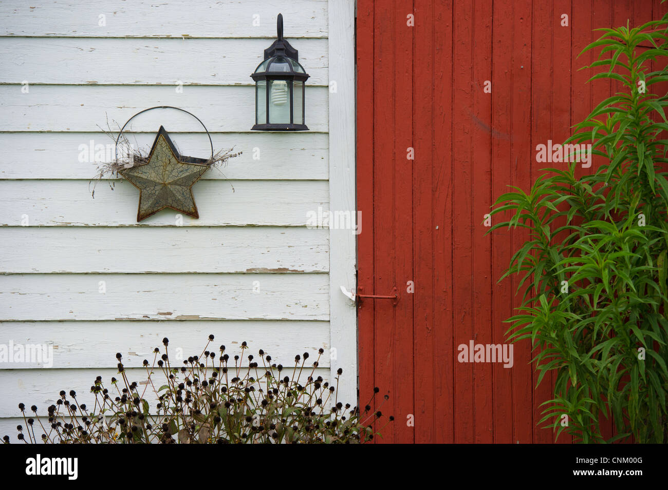 Décoration étoile et lampe sur le côté d'une grange blanche avec une porte rouge. Banque D'Images