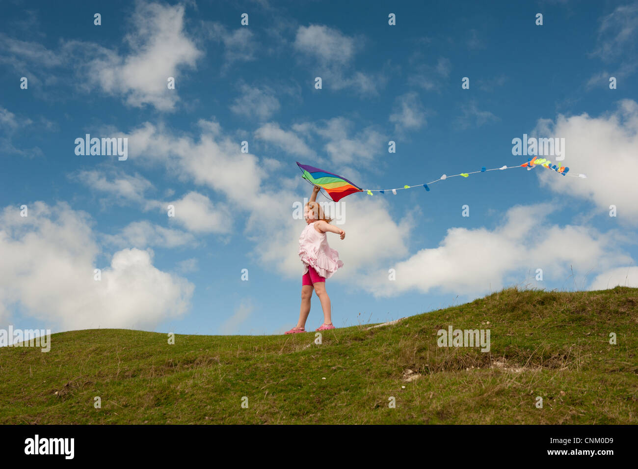 Une fille aux cheveux rouges avec un arc-en-ciel cerf-volant sur Maiden Castle, Dorchester, Dorset Banque D'Images