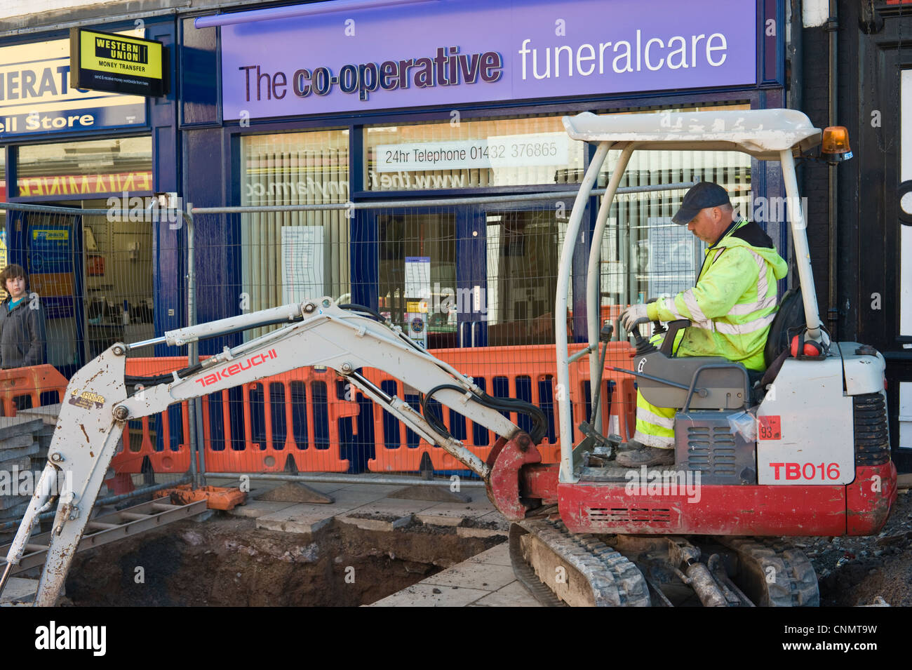 L'homme à l'extérieur du trou d'excavation mini digger CO-OPERATIVE FUNERALCARE en centre-ville de Hereford Herefordshire Angleterre UK Banque D'Images