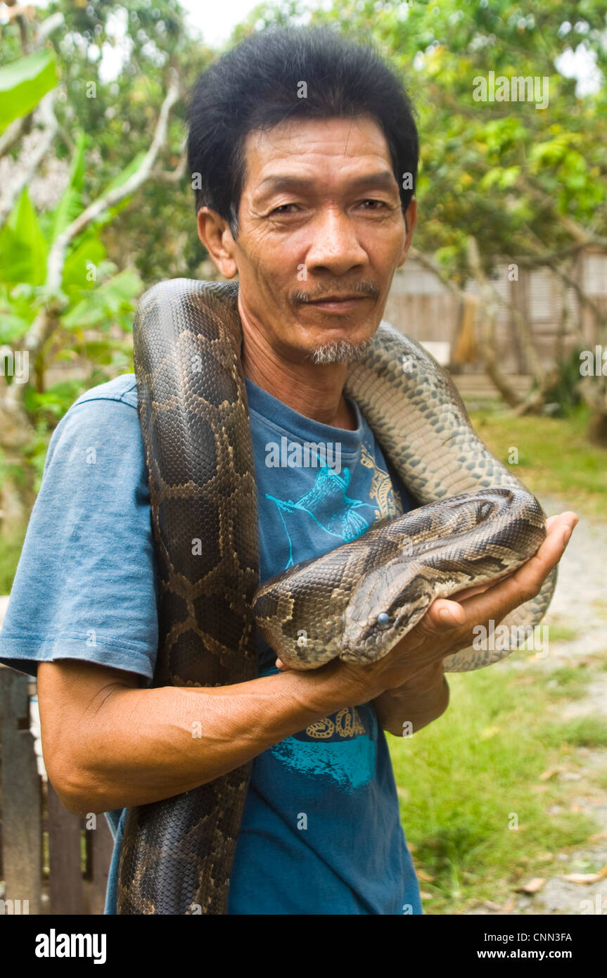 Vue verticale d'un agriculteur vietnamien holding avec amour son animal Boa constrictor serpent. Banque D'Images