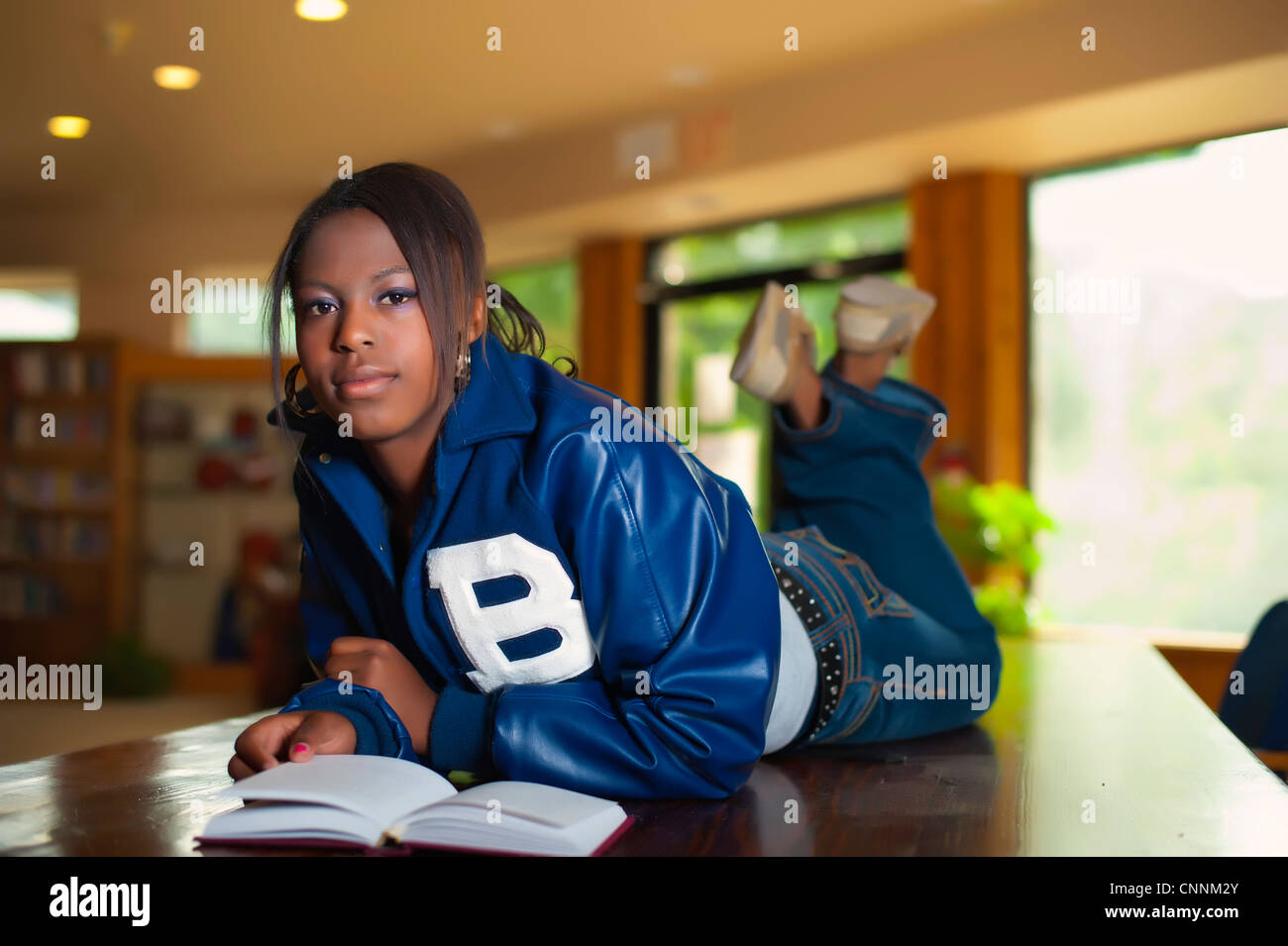 Young woman reading book couchée sur son ventre dans une bibliothèque Banque D'Images