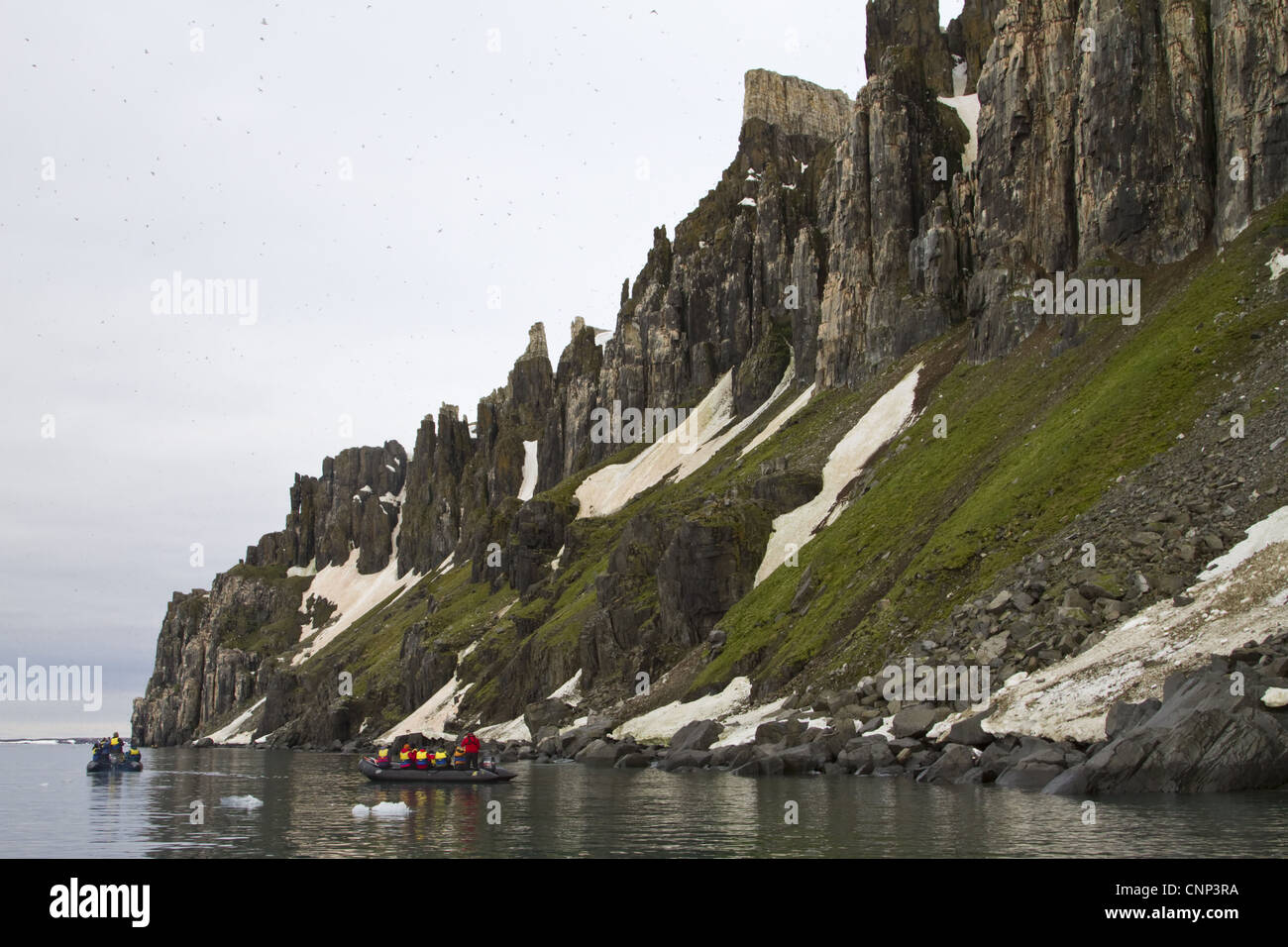 Les touristes en bateaux gonflables Zodiac ci-dessous de hautes falaises, Alkenfjellet, Spitzberg, Svalbard, juillet Banque D'Images