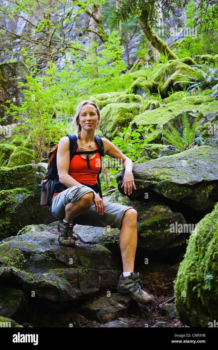 Une femme qui pose pour un portrait sur un sentier rocheux entre des roches couvertes de mousse, si peu de trail, Washington, USA. Banque D'Images