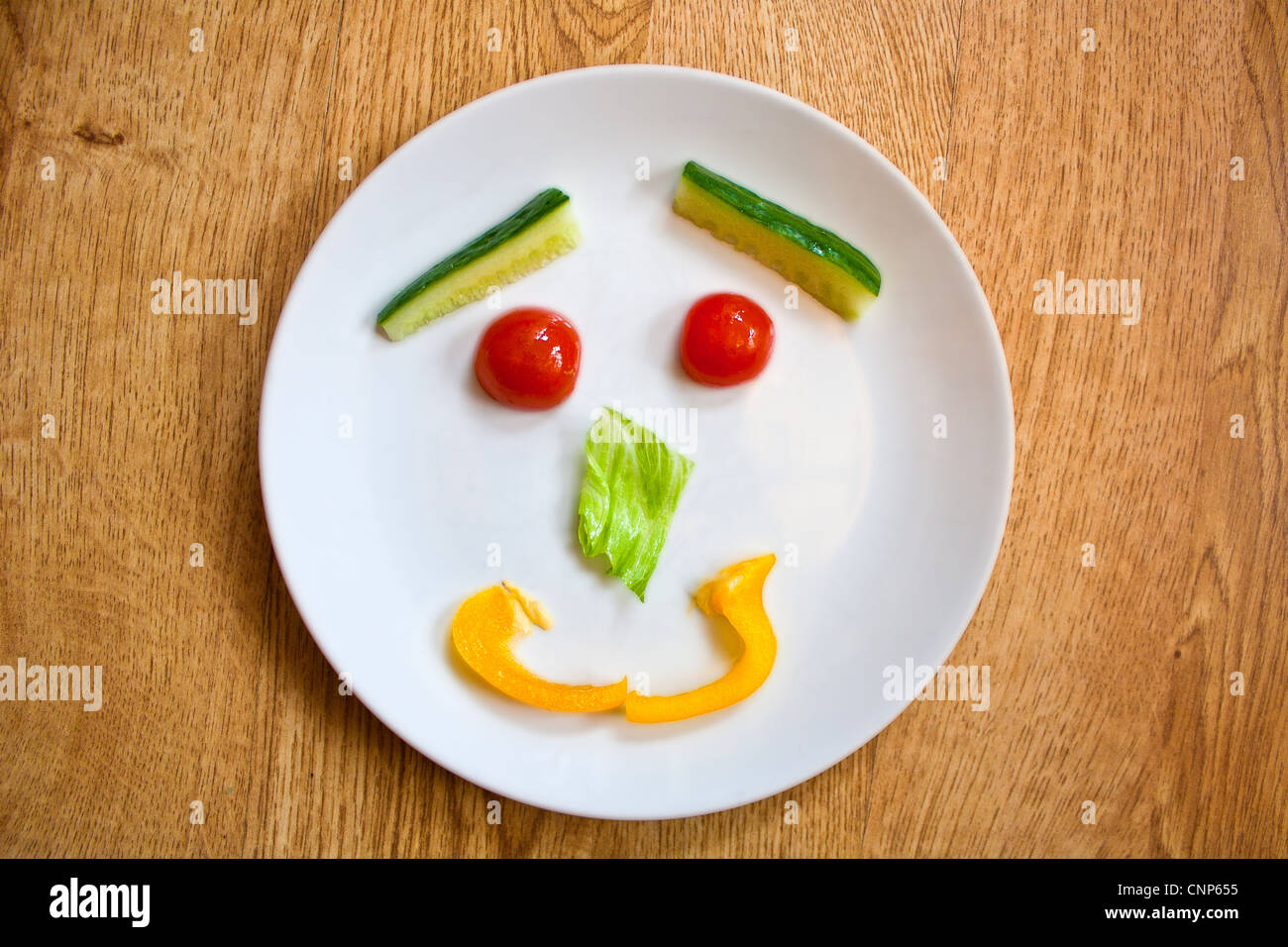 Assiette de salade saine affiché dans un smiley à l'aide de concombres, tomates cerises, la laitue et le poivron jaune. Banque D'Images