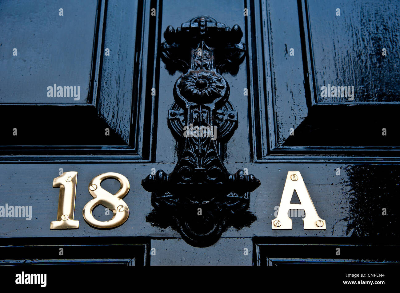 Panneaux en bois peint noir porte avant avec un fer à repasser heurtoir, numéro 18 et une lettre en laiton Banque D'Images