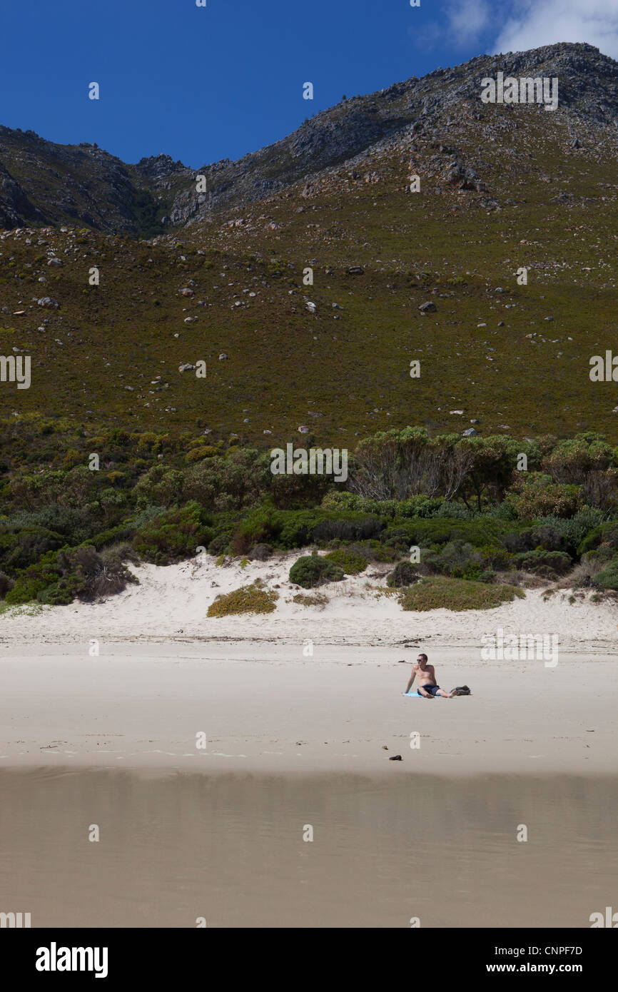 Un homme assis dans le sable sur la plage, à Kogel Bay, Western Cape, Afrique du Sud Banque D'Images