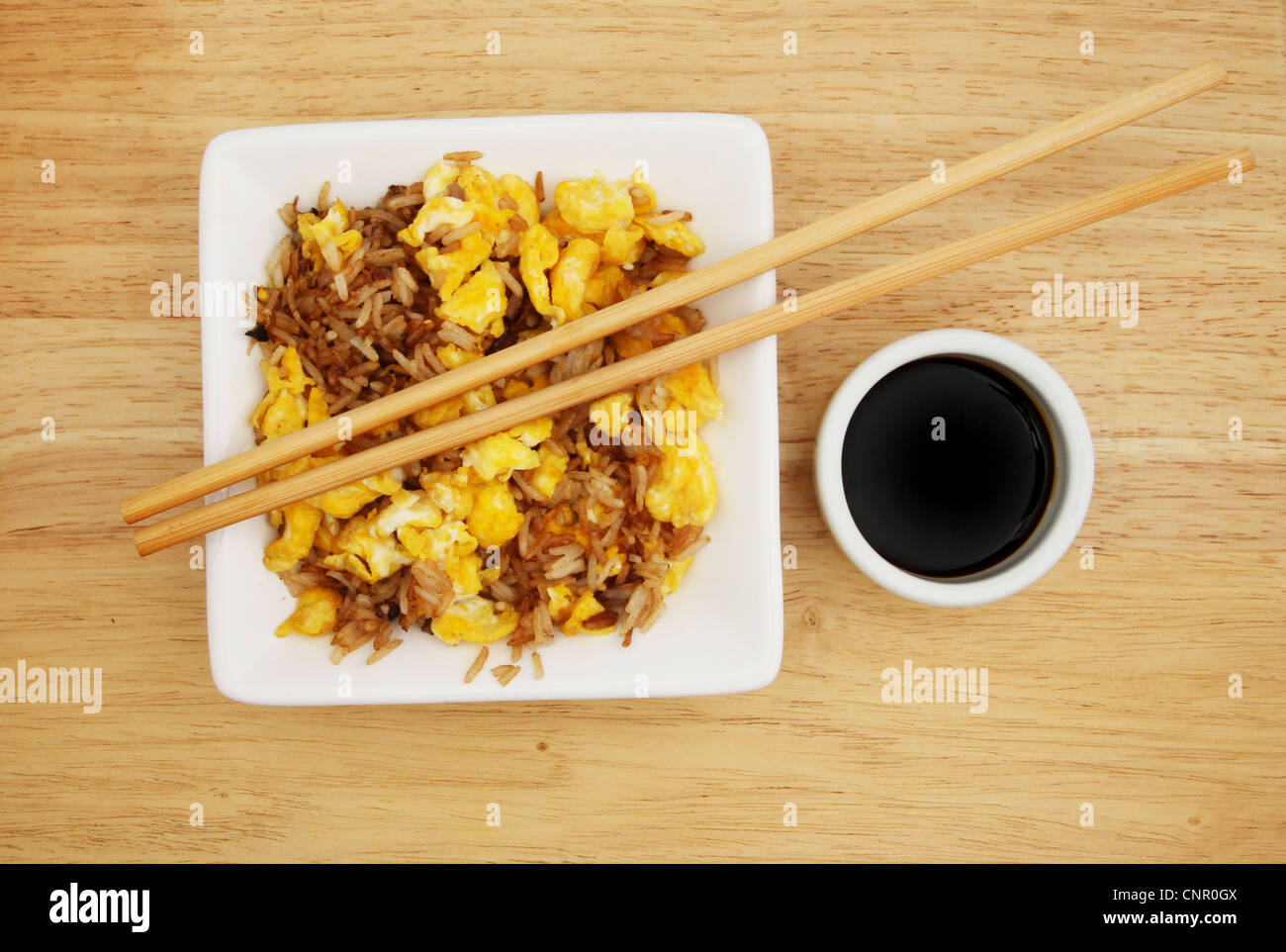 Riz frit à l'oeuf dans un bol carré avec des baguettes et un bol de sauce de soja sur une surface en bois Banque D'Images