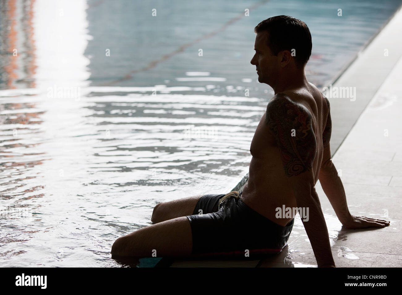 L'homme se balançant les jambes dans la piscine Banque D'Images
