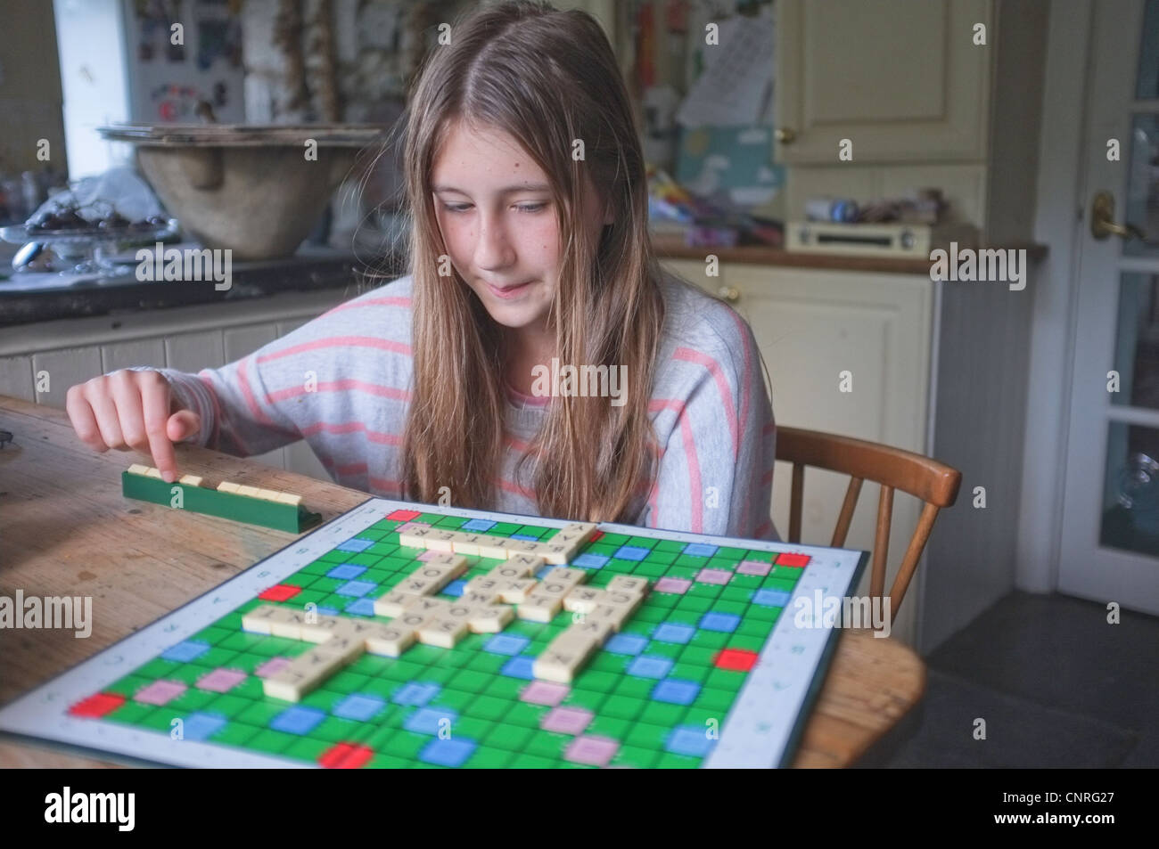 Une jeune fille de 11 ans jouant au Scrabble dans une cuisine Banque D'Images