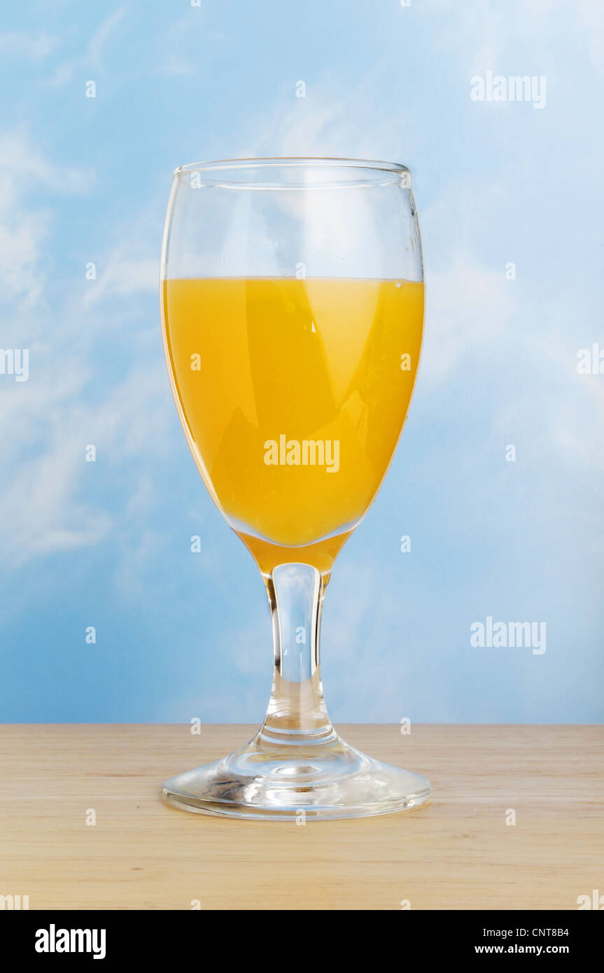 Jus d'orange dans un verre de la tige sur une surface en bois contre un ciel bleu Banque D'Images