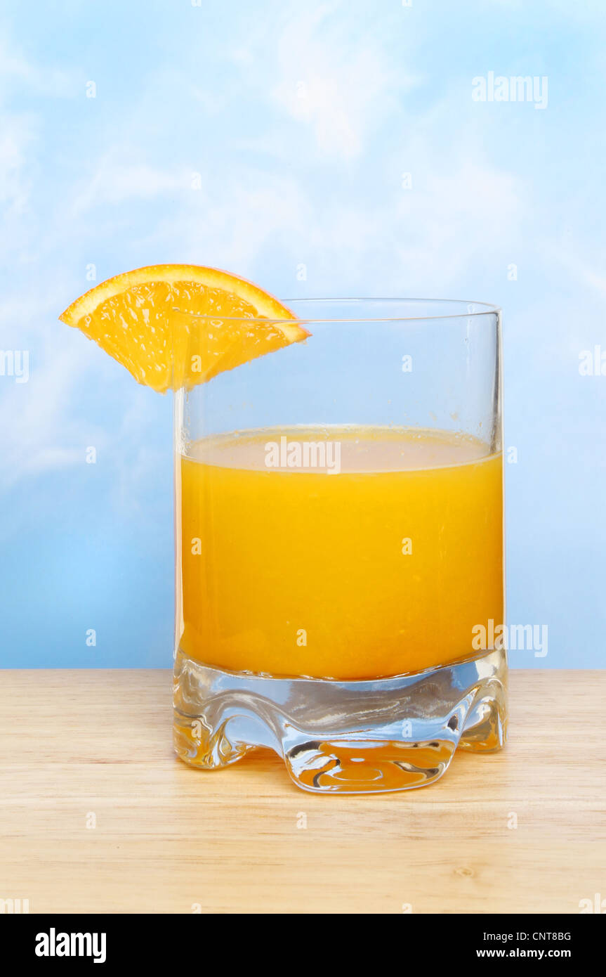 Le verre de pur jus d'orange fraîchement pressé sur une surface en bois contre un ciel bleu Banque D'Images