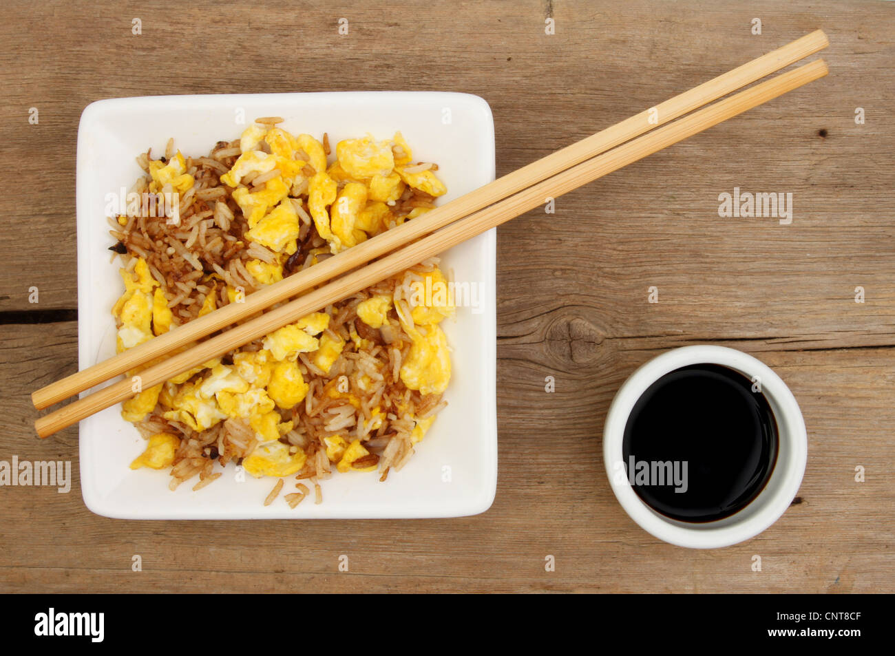 Bol de riz frit à l'oeuf avec des baguettes et un bol de sauce de soja sur une surface de bois patiné Banque D'Images