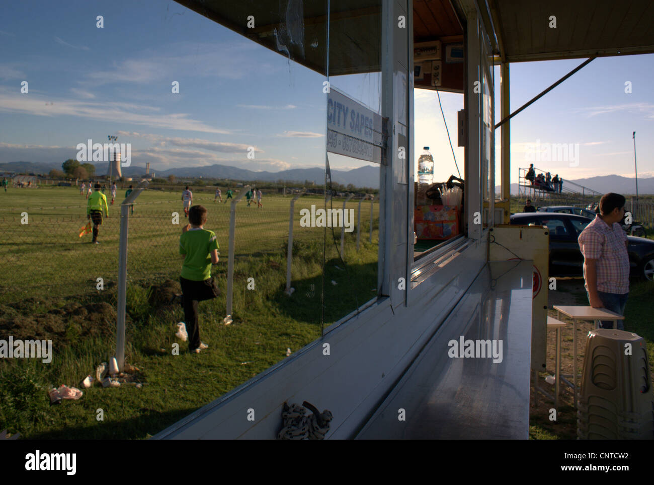Un match de football amateur reflétée sur un hot-dog van;'s miroir, avec des ventilateurs dans la distance de regarder le match. La Thrace, la Grèce. Banque D'Images