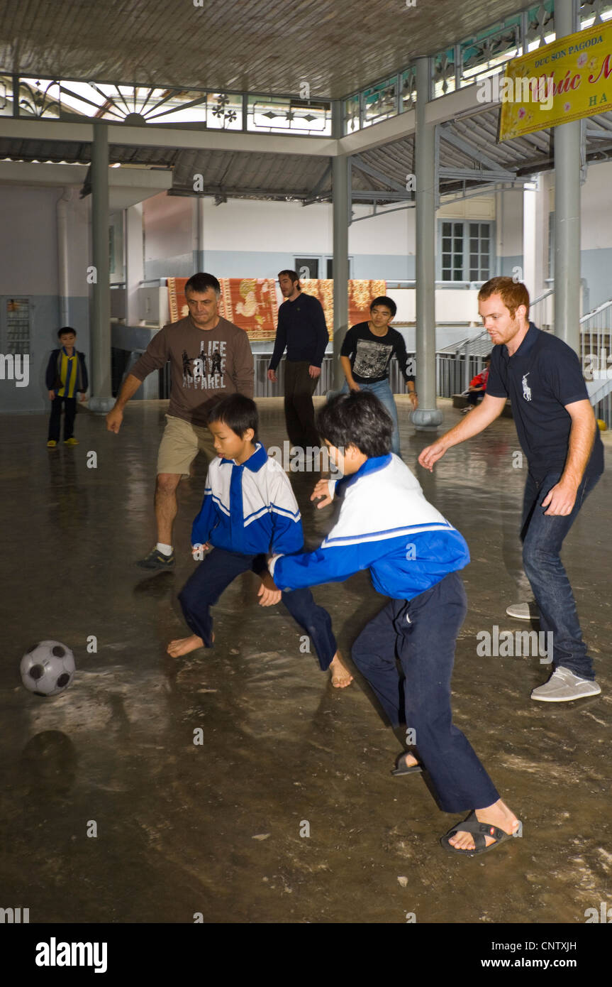 Vue horizontale des enfants vietnamiens s'amusant de jouer à un jeu de football avec des touristes occidentaux, dans un orphelinat près de Hue, Vietnam Banque D'Images