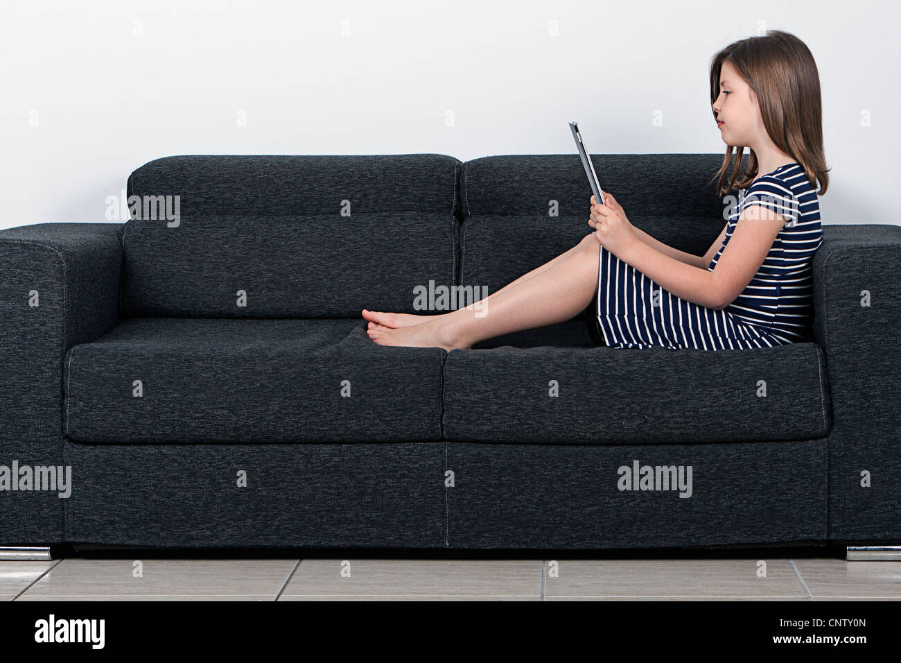 Girl Using Tablet Computer on Sofa Banque D'Images