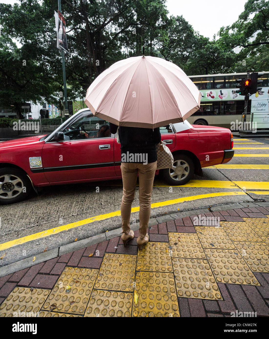 Une femme debout sur un coin de rue à Hong Kong sous la pluie, exerçant son activité sous un parapluie, comme un taxi drives passé Banque D'Images