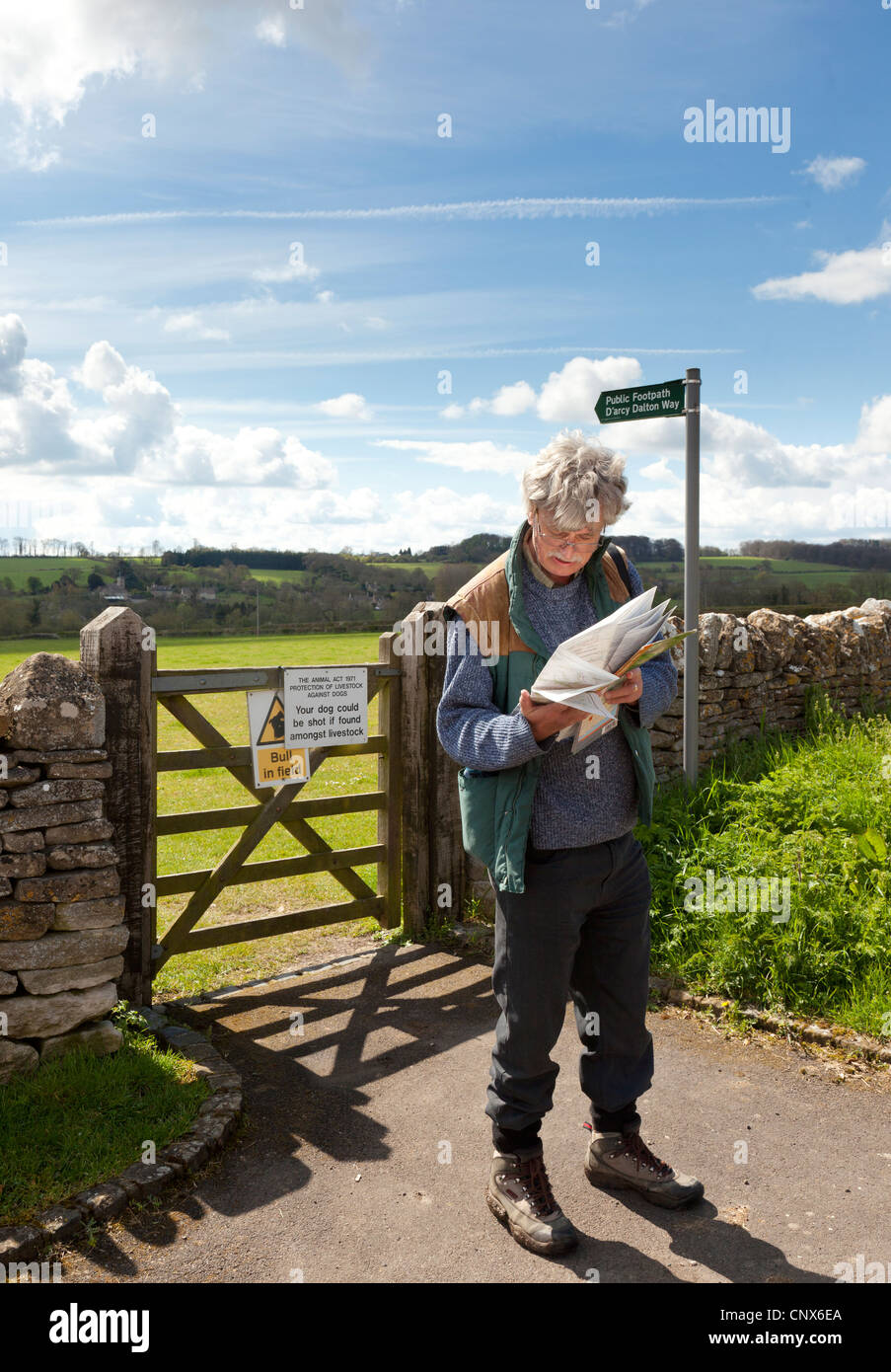 Un Walker de la lecture d'un site à côté d'une barrière sur le chemin d'arcy Dalton dans le village des Cotswolds de Great Barrington, Gloucestershire Banque D'Images