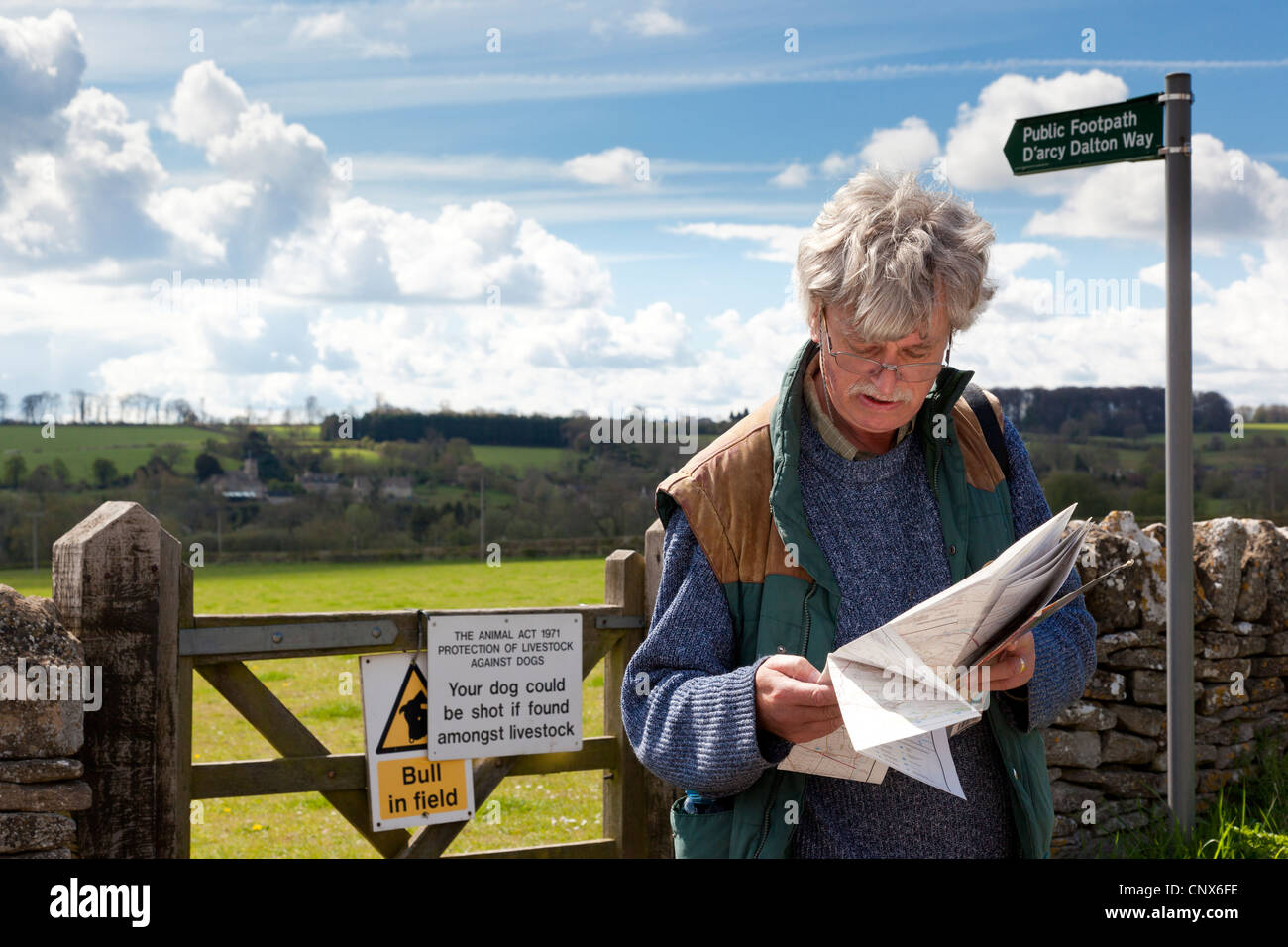 Un Walker de la lecture d'un site à côté d'une barrière sur le chemin d'arcy Dalton dans le village des Cotswolds de Great Barrington, Gloucestershire Banque D'Images