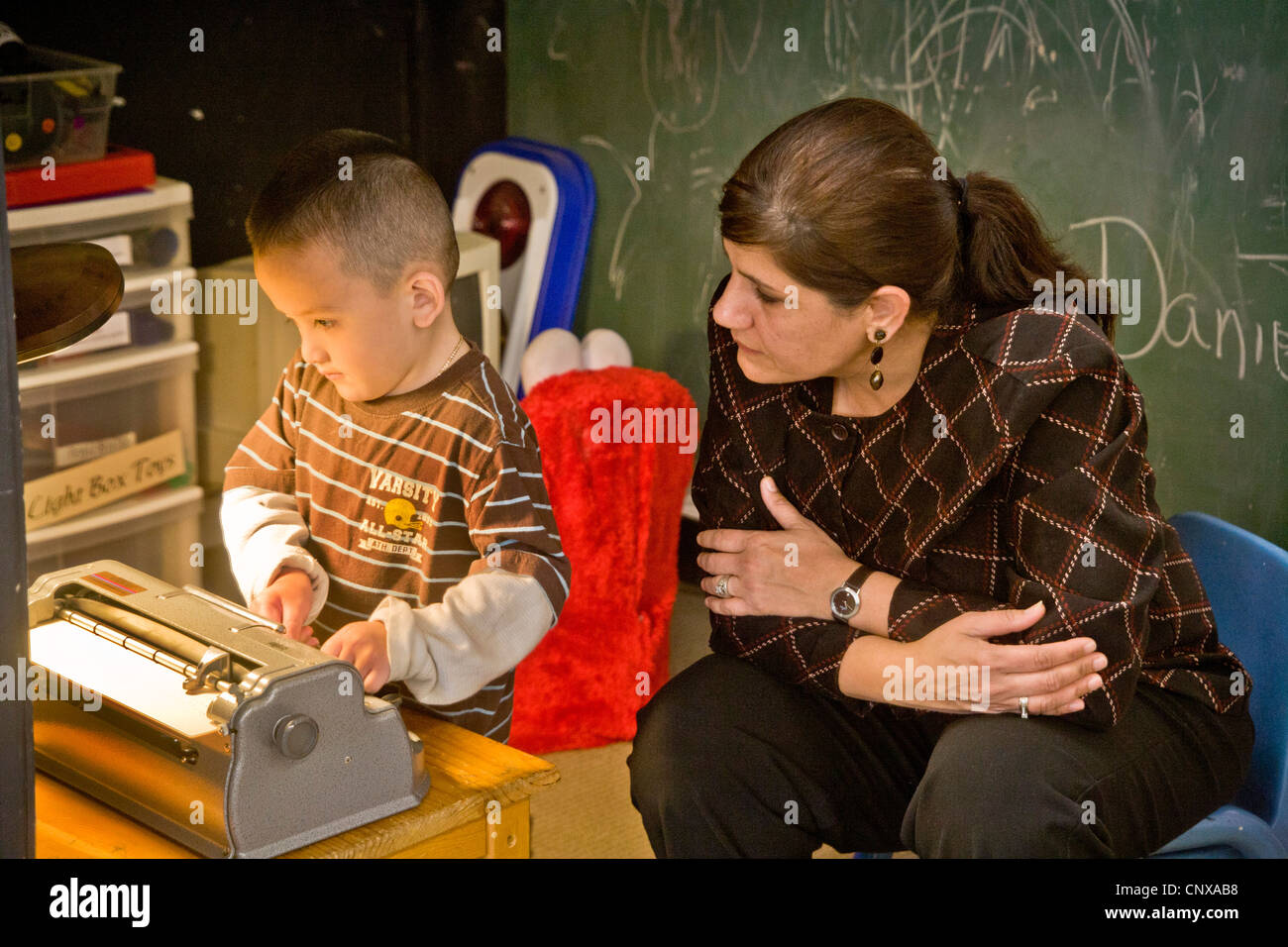 Avec l'aide d'un membre du personnel formé un garçon aveugle sur une machine à écrire braille types à l'intention des enfants aveugles Centre d'apprentissage. Banque D'Images