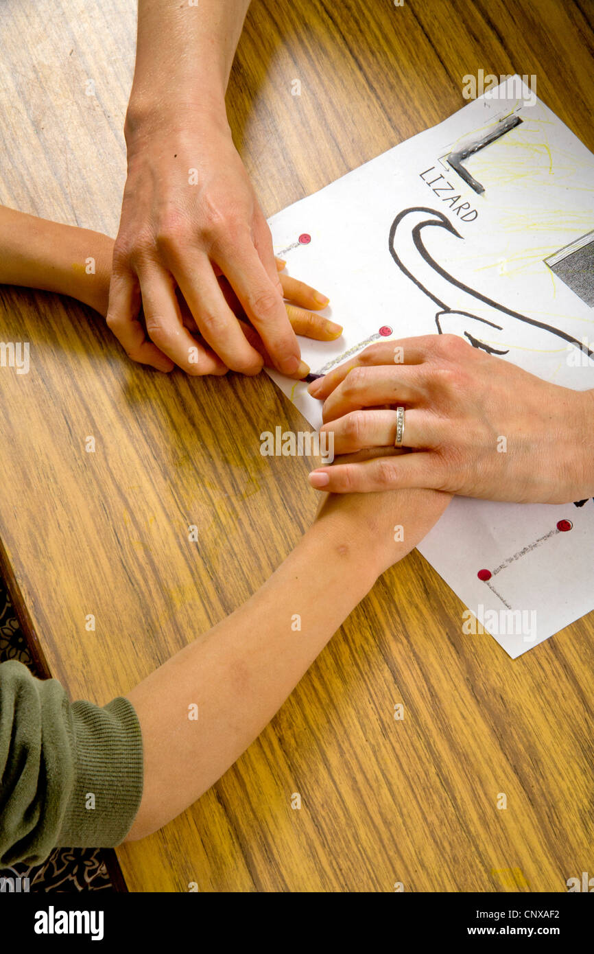 Un des guides de l'enseignant un enfant aveugle, les mains sur les grandes lignes d'un lézard dans soulevées dans un type de classe d'écriture des besoins spéciaux. Banque D'Images