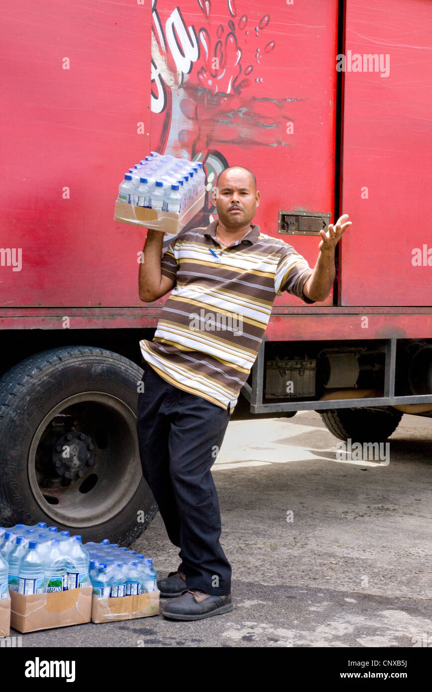 Un conducteur offrant de l'eau en bouteille à un village supermarché pose pour une photo à Calibishie Dominique Banque D'Images