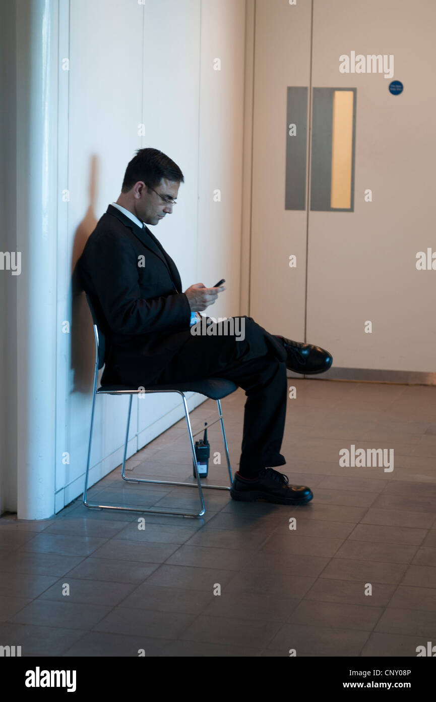 London City Hall Southbank security guard assis sur une chaise de lecture contrôle mobile cell phone avec radio talkie walkie marbre oublieux environs Banque D'Images