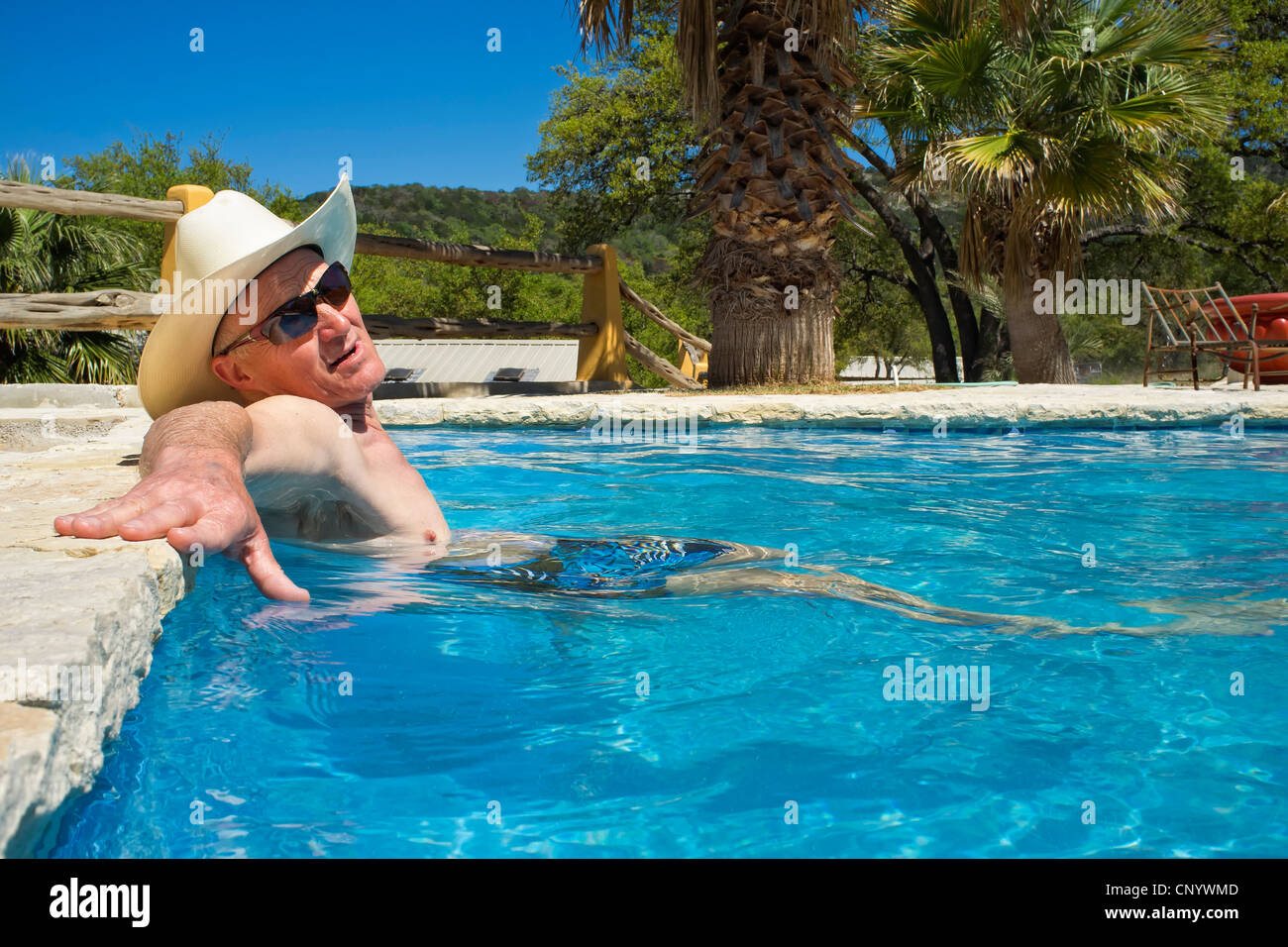 Homme d'âge moyen avec des lunettes de soleil et chapeau de cow-boy et rafraîchissant dans une piscine de détente Banque D'Images