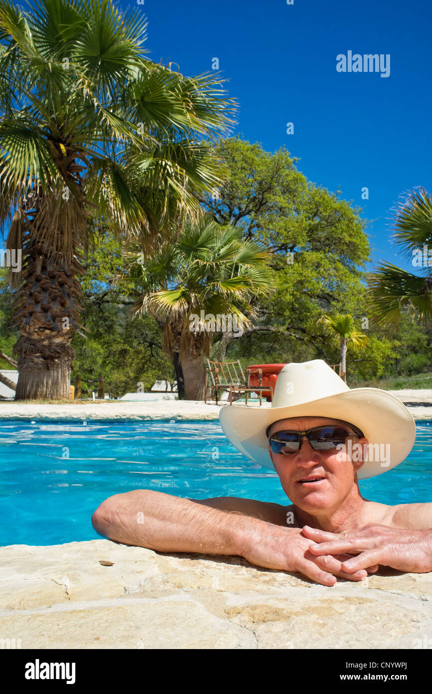 Homme d'âge moyen avec des lunettes de soleil et chapeau de cow-boy et rafraîchissant dans une piscine de détente Banque D'Images