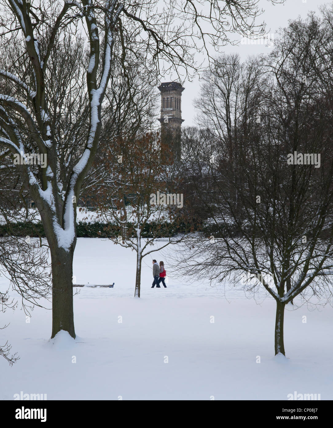 Couple en train de marcher dans la neige couverts Lister Park, Bradford, Lister avec tour de l'usine à l'arrière-plan. Banque D'Images