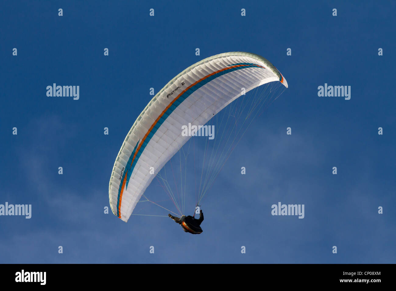 Un parapentiste avec un blanc rouge et bleu aile, contre un ciel bleu avec des nuages pâles. Banque D'Images