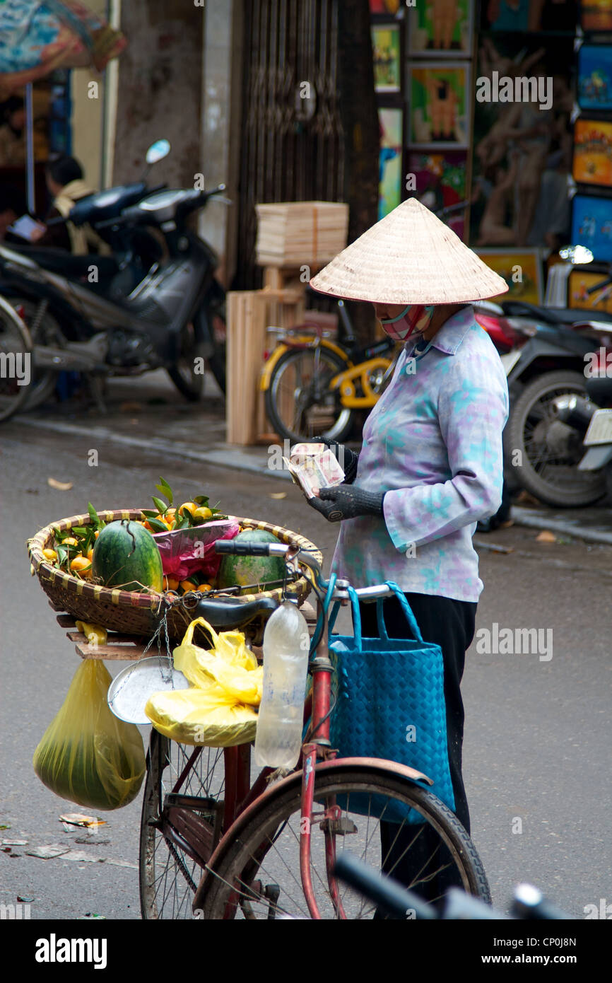 Un vendeur de fruits en comptant ses gains à Hanoi Old Quarter. Banque D'Images