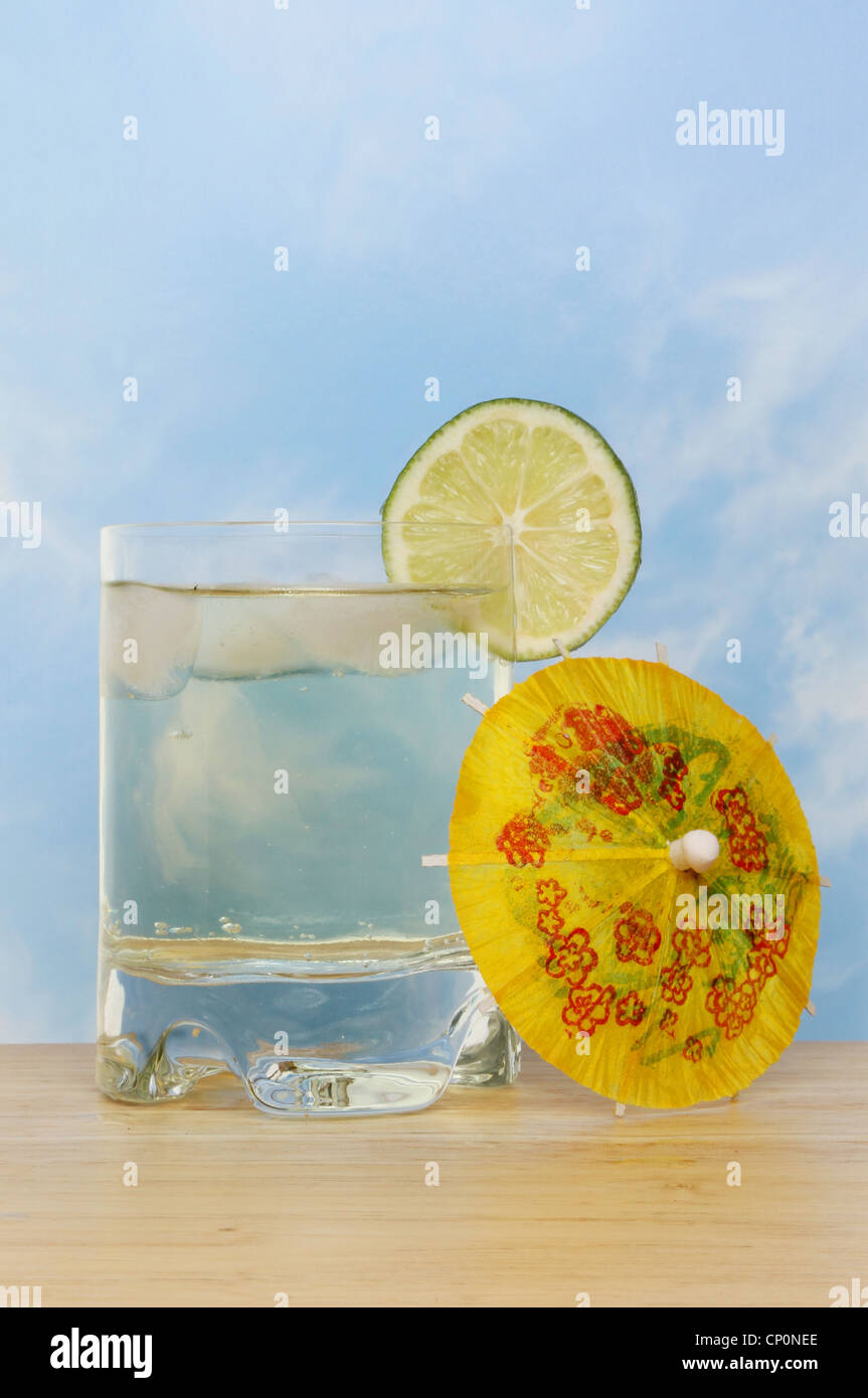 Cool et rafraîchissante boisson à saveur de citron vert avec une tranche de lime et un cocktail umbrella against a blue sky Banque D'Images