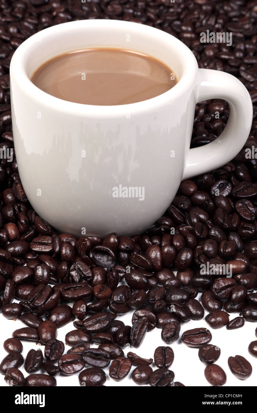 Photo d'une tasse en céramique pleine de café chaud entouré d'un mélange de grains de café arabica et robusta. Banque D'Images