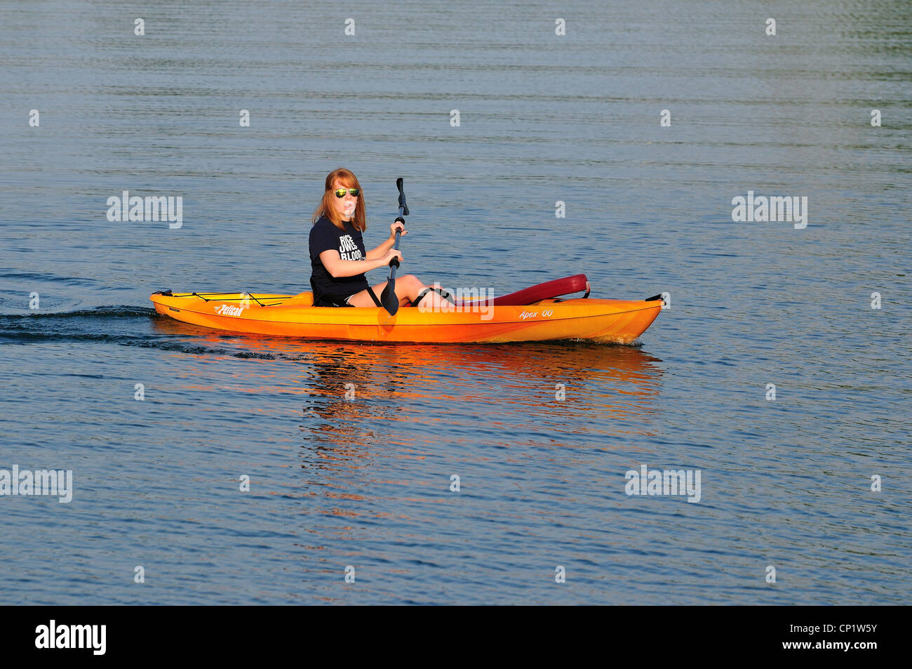 Une jeune femme à travers la palette d'un lac sur une orange en kayak. Banque D'Images