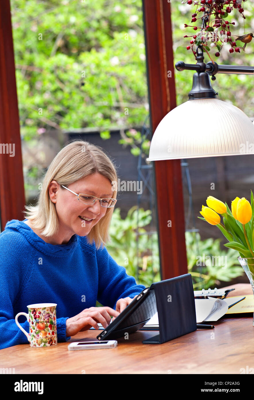 Femme blonde travailler à domicile dans son jardin d'hiver à l'aide de l'ordinateur tablette iPad dans son cache du socle en cuir Banque D'Images