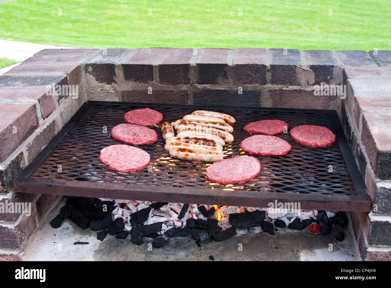 Des hamburgers et des saucisses cuisson sur un barbecue en brique Banque D'Images