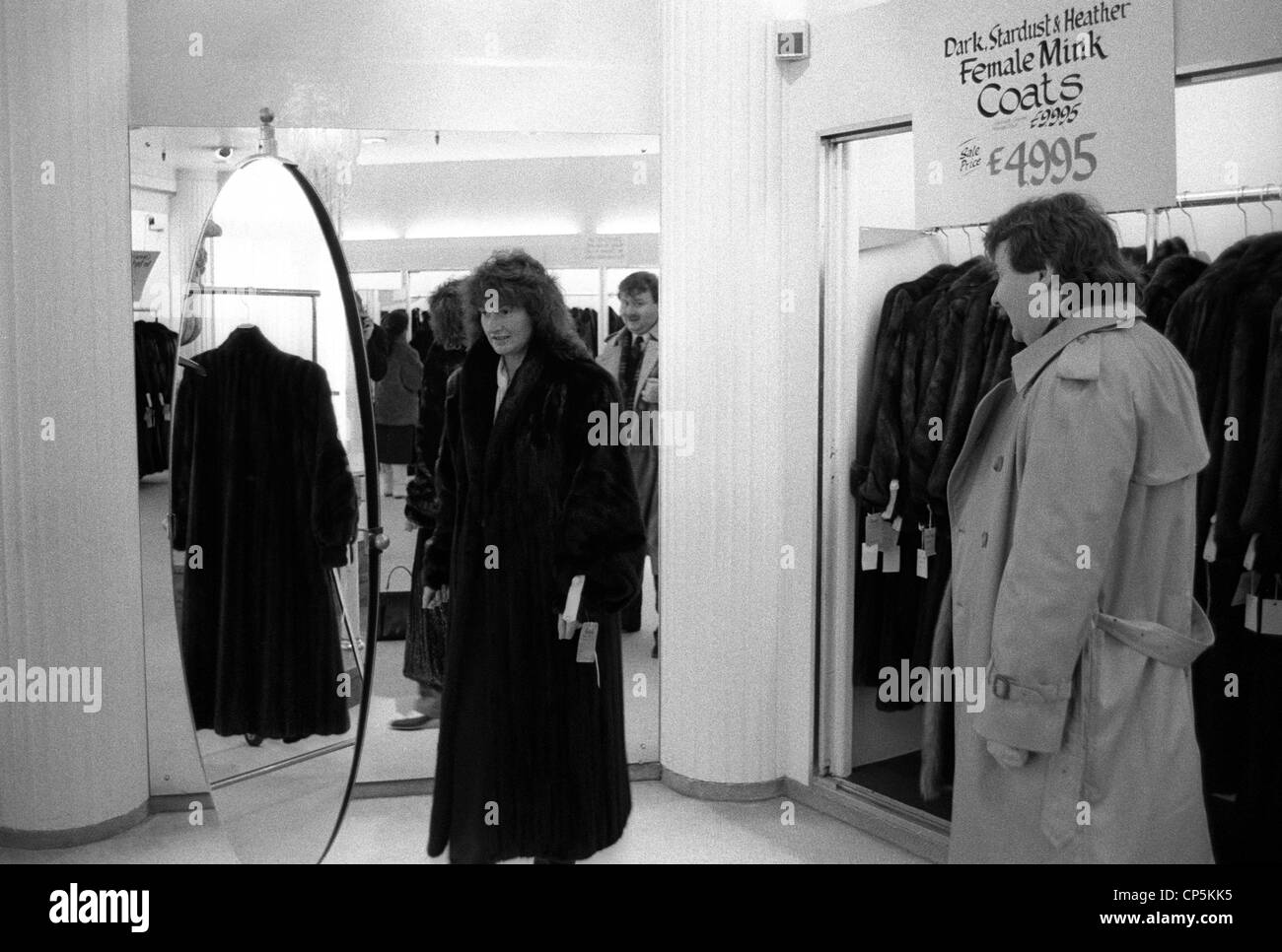 Dans la zone de changement d'un grand magasin, sous le regard de son mari une femme essaie sur un manteau de fourrure Banque D'Images