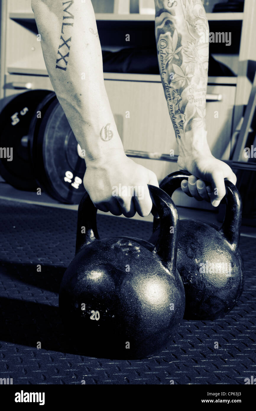 Bras tatoués kettlebells de levage à la gym pendant une session crossfit Banque D'Images