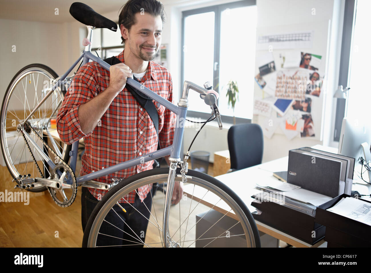 Germany, Cologne, young man carrying bicycle, smiling Banque D'Images