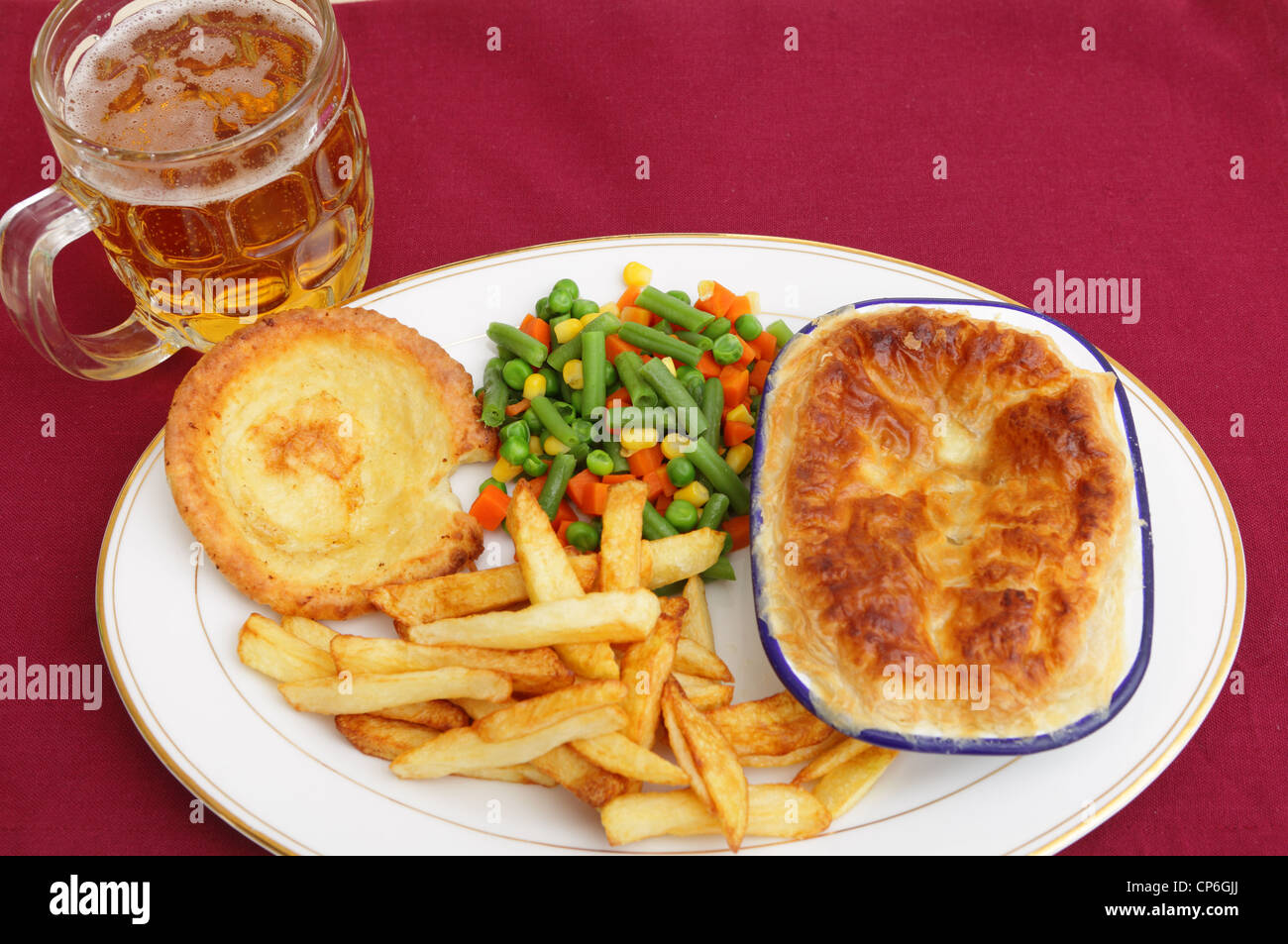 Un repas de style pub d'une tarte de viande servi avec un mélange de légumes, frites, Yorkshire pudding et un verre de bière blonde. Banque D'Images