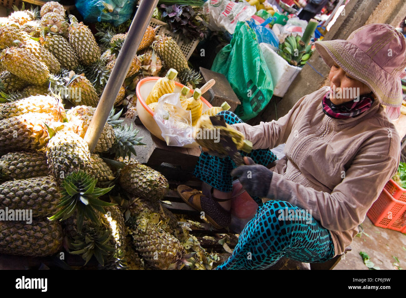 Vue horizontale d'une pauvre dame vietnamienne de la préparation d'ananas pour la vente à un aliment traditionnel et marché aux fleurs à Hoi An, au Vietnam. Banque D'Images