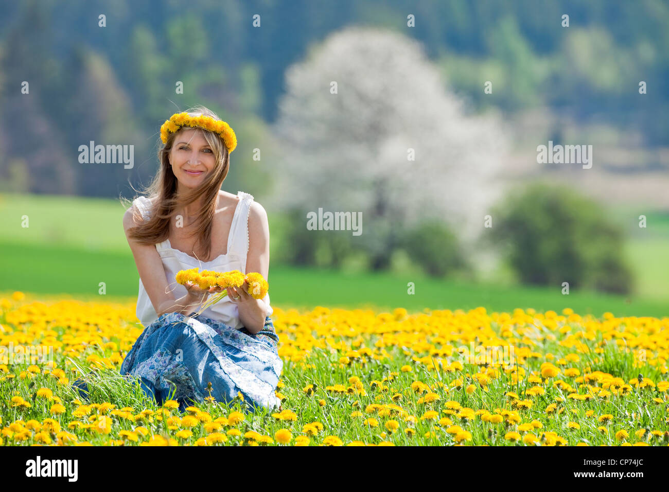 Femme assise dans un champ de pissenlit, smiling at camera Banque D'Images