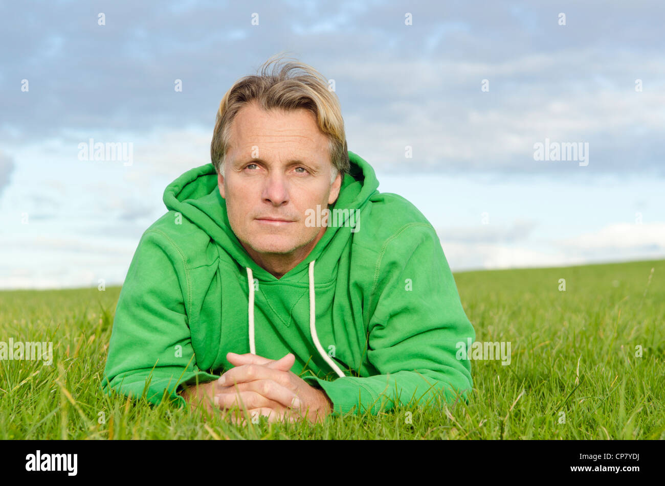 Un portrait d'un homme mûr à la rêveuse aux cheveux blonds portant sur l'herbe et portant un haut vert. Banque D'Images