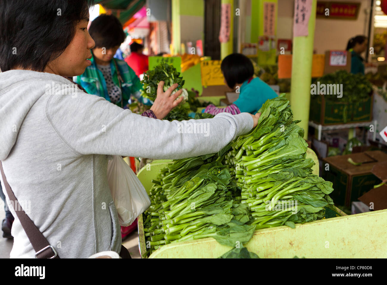 Une femme d'atteindre pour le brocoli chinois au marché - San Francisco, California USA Banque D'Images